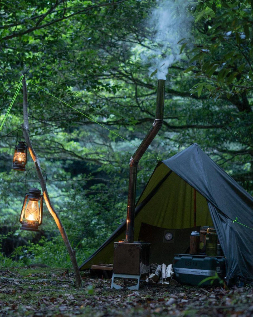 Green oilskin tarp shelter with hanging lanterns in woodland