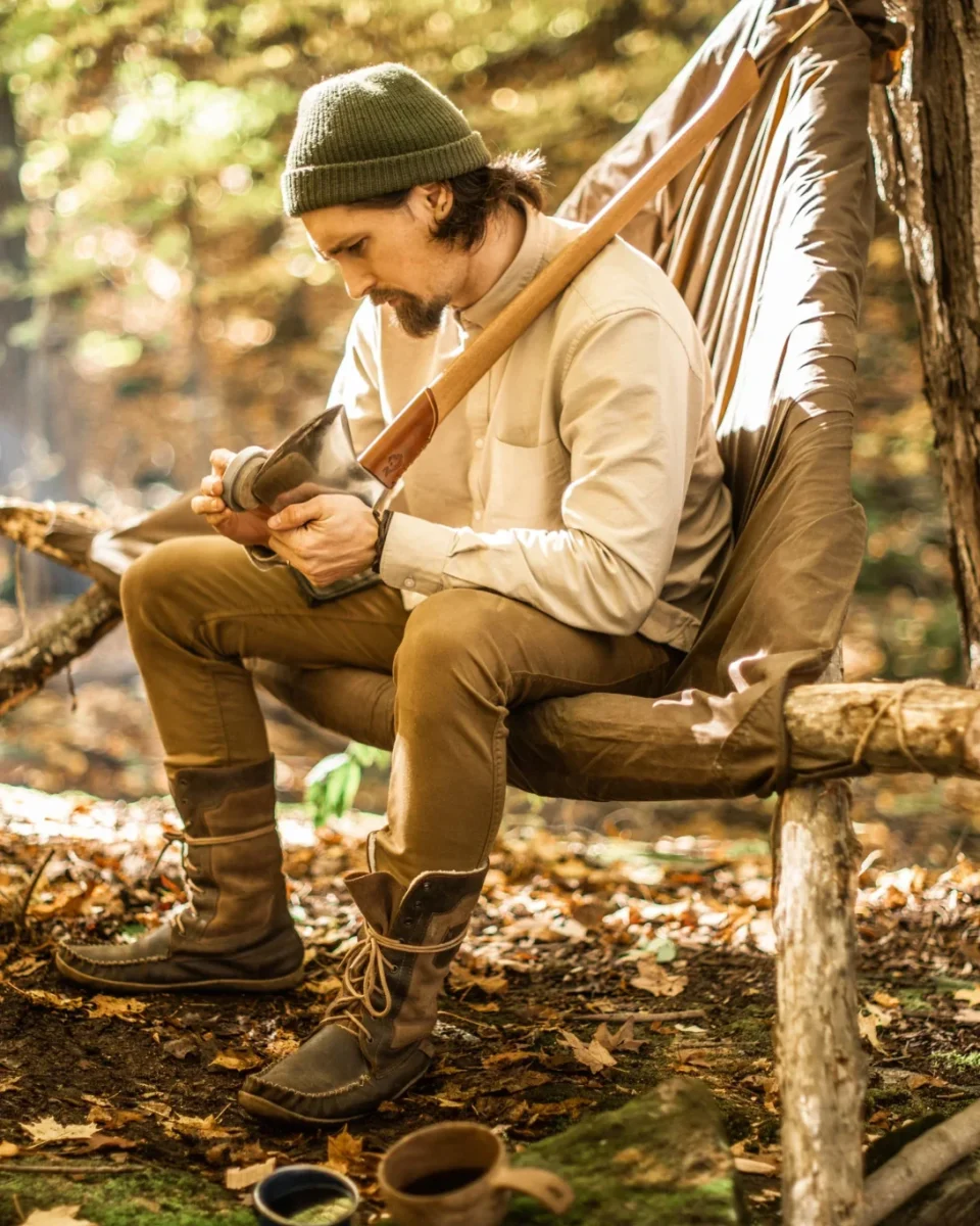 Bushcrafter sharpening a Jauregi Basque axe with a round sharpening stone while seated at camp.