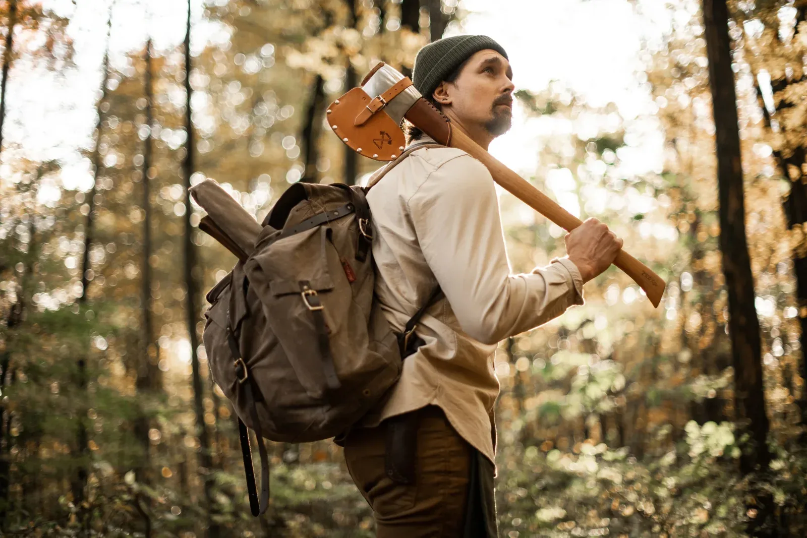 Bushcrafter carrying an axe with a leather sheath through an autumn woodland