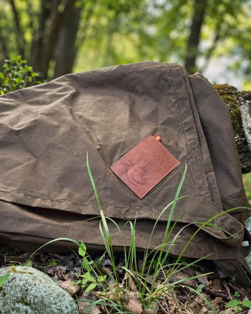 Folded brown Genuine Nessmuk oilskin tarp with the Bushcraft Spain leather label in a woodland setting