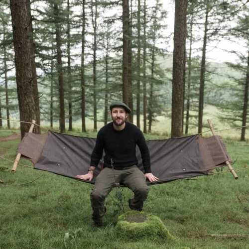 Camper sitting on a Kephart Roll camp cot in woodland