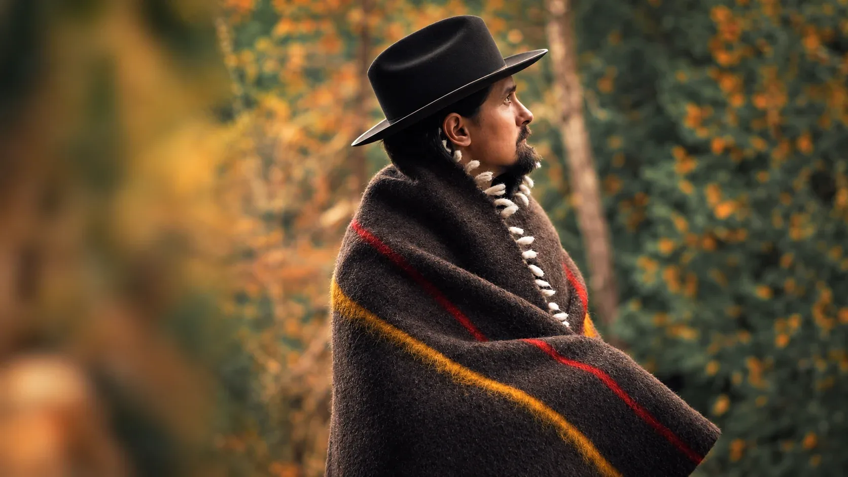 Brown merino wool blanket with red and yellow stripes worn in the forest