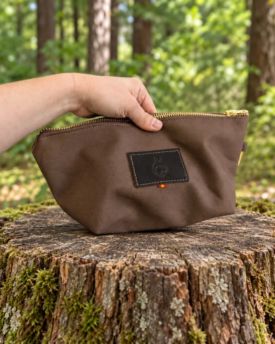 Brown oilskin travel bag held by hand above a tree stump