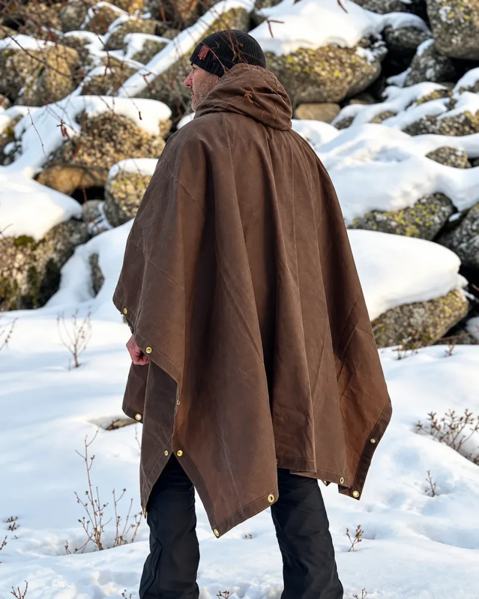 Rear view of the brown Oilskin Poncho Shelter with hood in a snowy landscape