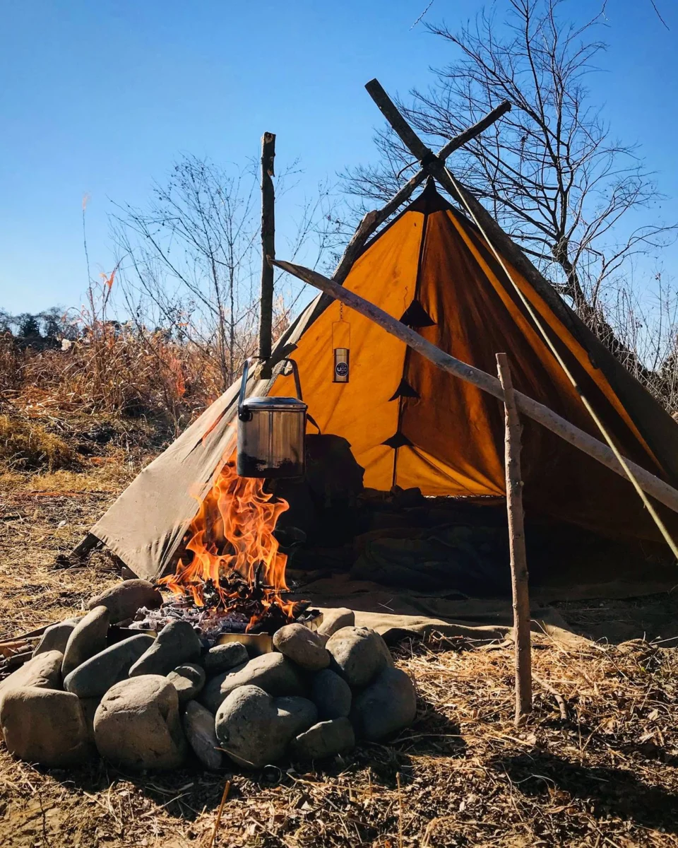 Oilskin tarp pitched on a wooden frame beside a campfire
