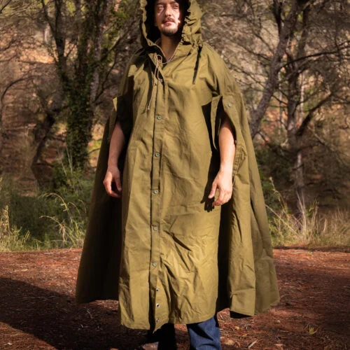 Vista frontal de cuerpo entero de la réplica del poncho del ejército polaco de lona de algodón verde oliva, con la capucha puesta, en el bosque.