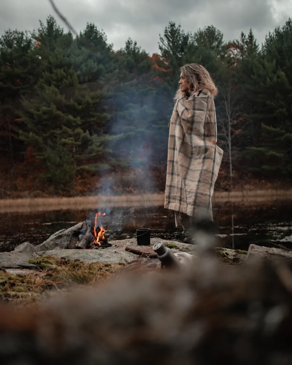 Careena Alexis con el poncho de lana Shetland a cuadros junto a una hoguera a orillas de un lago